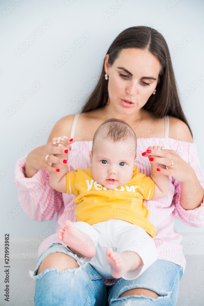 happy mom sits on the floor with her little son on a gray background happy mom sits on the floor with her little son on a gray background