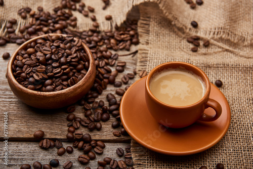 coffee beans in bowl near cup of coffee on wooden background