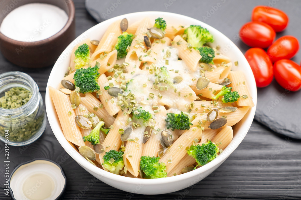 Bowl with pasta, green onions, white sauce, pumpkin seeds and broccoli. On the table are cherry tomatoes, salt, green onions. Bowl with pasta, green onions, white sauce, pumpkin seeds and broccoli. On the table are cherry tomatoes, salt, green onions.