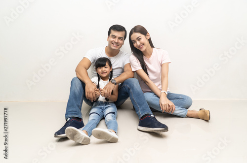 Father, mother and cute daughter. Beautiful and happy multiethnic smiling young family are hugging and have a fun time together while sitting on the floor and looking on camera. Family day