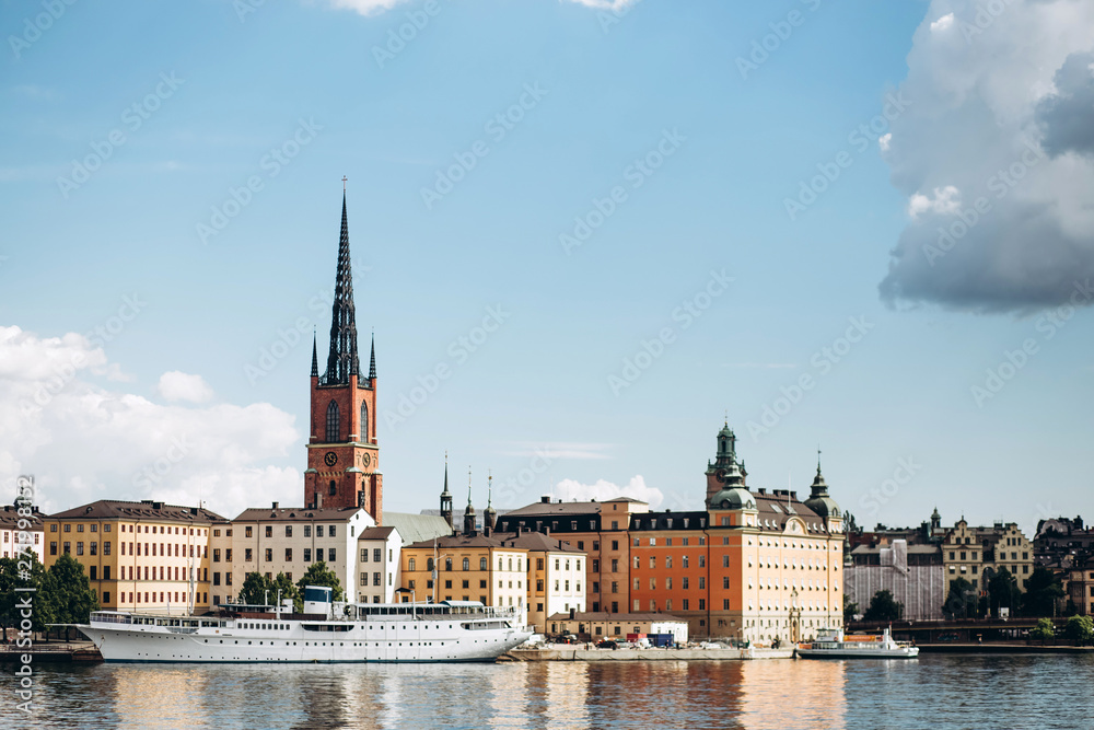 Scenic summer panorama of the Old Town (Gamla Stan) architecture in Stockholm, Sweden. view from Monteliusvagen hill on island Riddarholm and tower of church. Lake Malaren with blue sky, white clouds.