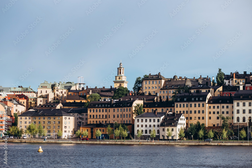 Fototapeta premium Scenic summer panorama of the Old Town (Gamla Stan) architecture in Stockholm, Sweden. view from Monteliusvagen hill on island Riddarholm and tower of church. Lake Malaren with blue sky, white clouds.