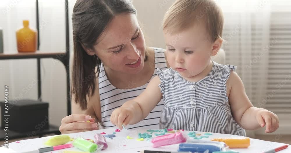 Mother kissing her baby daughter while playing with plasticine at home Mother kissing her baby daughter while playing with plasticine at home
