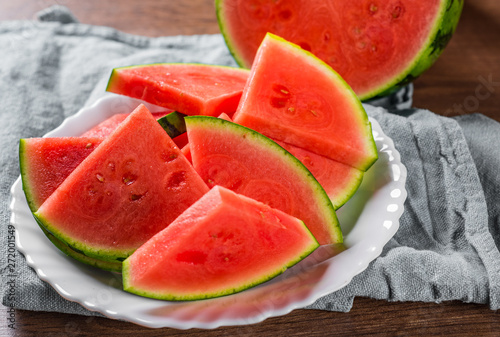 Cut slices of juicy watermelon on white plate on wooden table background