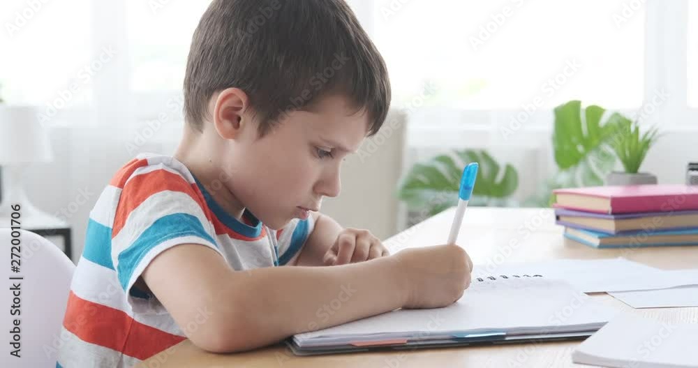 Boy writing in notebook while sitting at desk and doing homework Boy writing in notebook while sitting at desk and doing homework