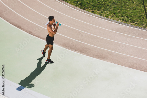mixed race sportsman holding towel and drinking water at stadium