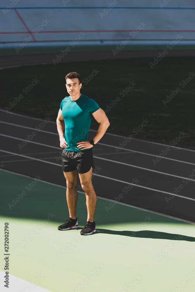 mixed race sportsman standing with hands on hips at stadium and looking at camera