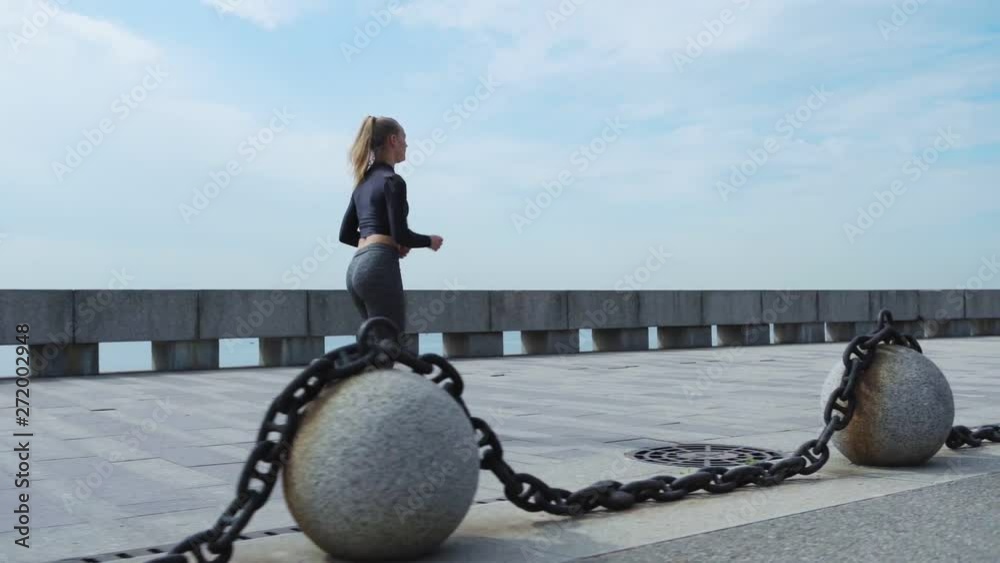 Side view tracking right shot of young female jogger running on promenade on summer day in slow motion