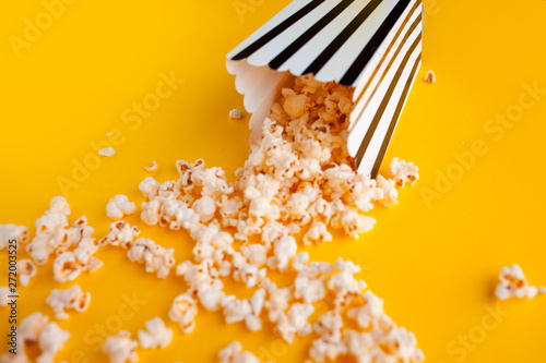 Popcorn in paper bag scattered on yellow background top view