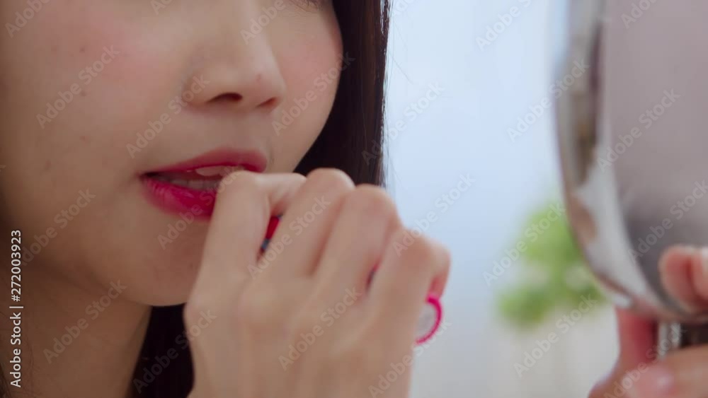 Young Asian woman using lipstick make up in front mirror, Happy female using beauty cosmetics to improve herself ready to working in bedroom at home. Lifestyle women at home concept. Slow motion shot. Young Asian woman using lipstick make up in front mirror, Happy female using beauty cosmetics to improve herself ready to working in bedroom at home. Lifestyle women at home concept. Slow motion shot.