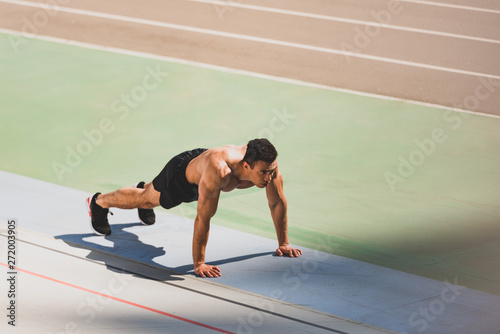 mixed race sportsman standing in plank at stadium