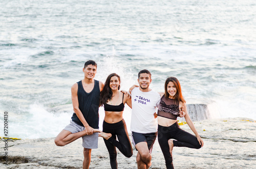 Group of people doing yoga exercises and smiling on the beach