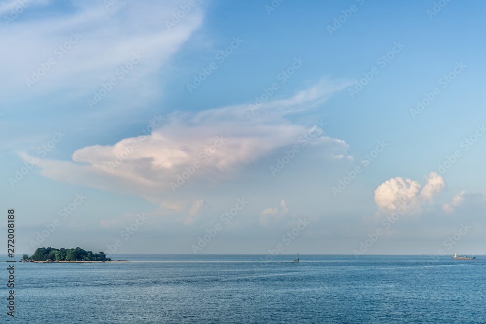 Makassar, Sulawesi, Indonesia - February 28, 2019: Small green Samalona Island lost in blue sea under blue sky with white cloudscape early morning. Ship on horizon.