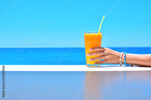 Fototapeta Naklejka Na Ścianę i Meble -  Cold orange fresh juice in female hand on a summer background with sea.