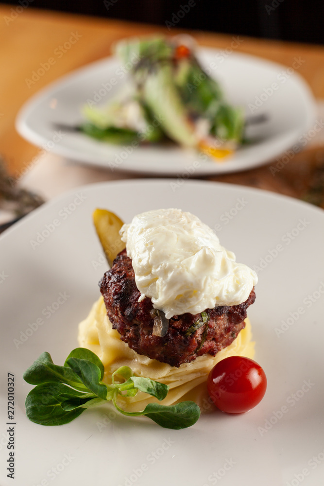 Close up of a meat cutlet, placed on a lay of fluffy mashed potatoes and served with white sauce and veggies Close up of a meat cutlet, placed on a lay of fluffy mashed potatoes and served with white sauce and veggies