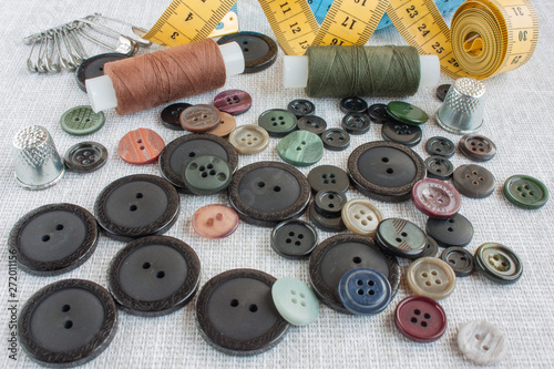 sewing tools: colored sewing threads, centimeter ribbons, thimbles, colored pins and buttons scattered on a light gray background close-up