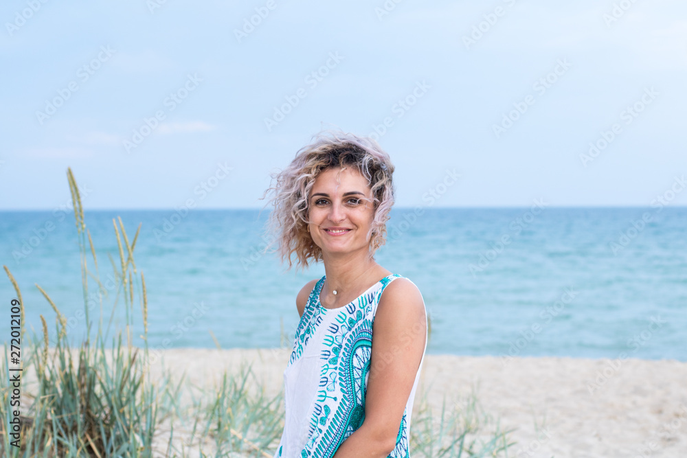 beautiful young woman with curly hairs in white dress with trasery is happy to be on the beach. Ocean and grass on the background beautiful young woman with curly hairs in white dress with trasery is happy to be on the beach. Ocean and grass on the background