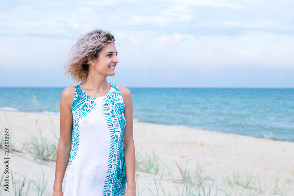 beautiful young woman with curly hairs in white dress with trasery is happy to be on the beach. Ocean and grass on the background beautiful young woman with curly hairs in white dress with trasery is happy to be on the beach. Ocean and grass on the background