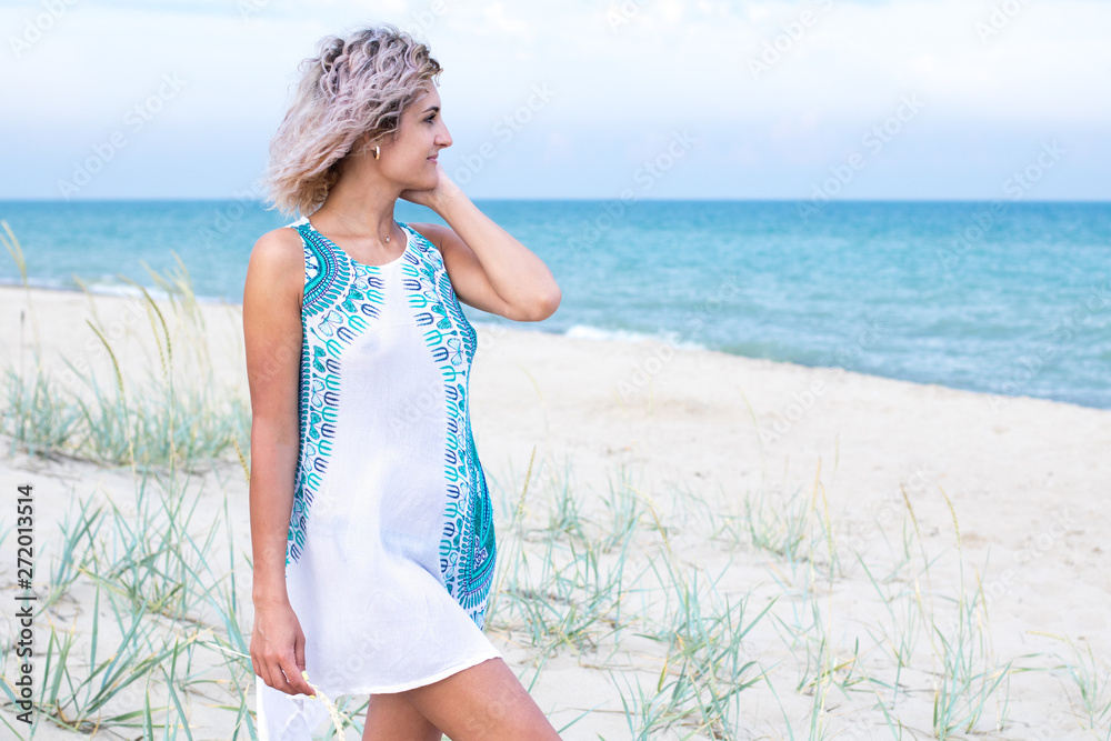 beautiful young woman with curly hairs in white dress with trasery is happy to be on the beach. Ocean and grass on the background beautiful young woman with curly hairs in white dress with trasery is happy to be on the beach. Ocean and grass on the background