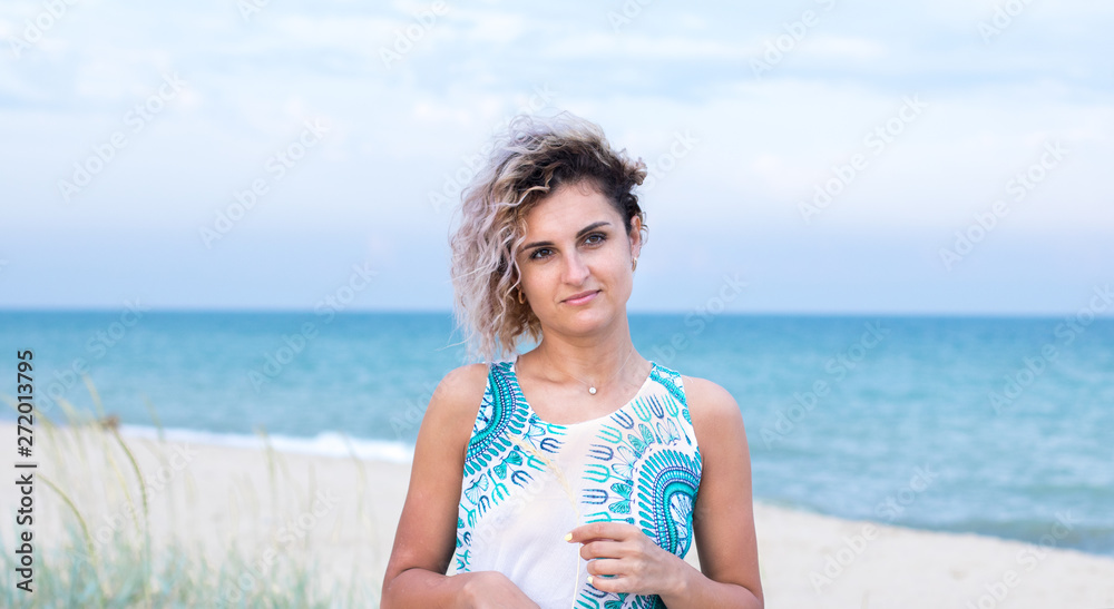 beautiful young woman with curly hairs in white dress with trasery is happy to be on the beach. Ocean and grass on the background beautiful young woman with curly hairs in white dress with trasery is happy to be on the beach. Ocean and grass on the background
