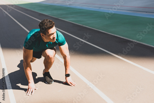 mixed race sportsman on start position looking away at stadium