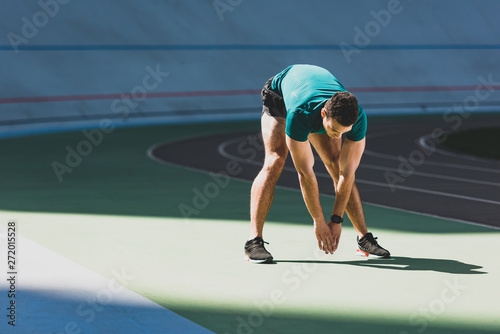 mixed race sportsman stretching at stadium, standing in sunlight on green floor