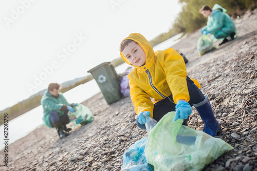 Small boy with green garbage clean near lake.