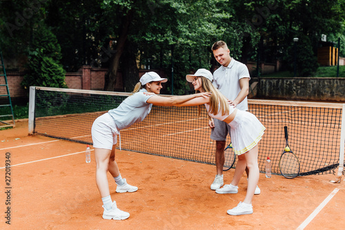 Attractive trainer help stretch to two female tennis player bending and touching their competition.
