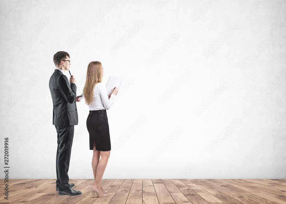 Fototapeta premium Businessman and businesswoman look at blank wall