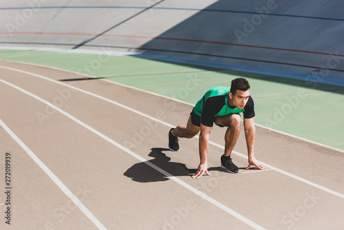 mixed race sportsman preparing to run at stadium