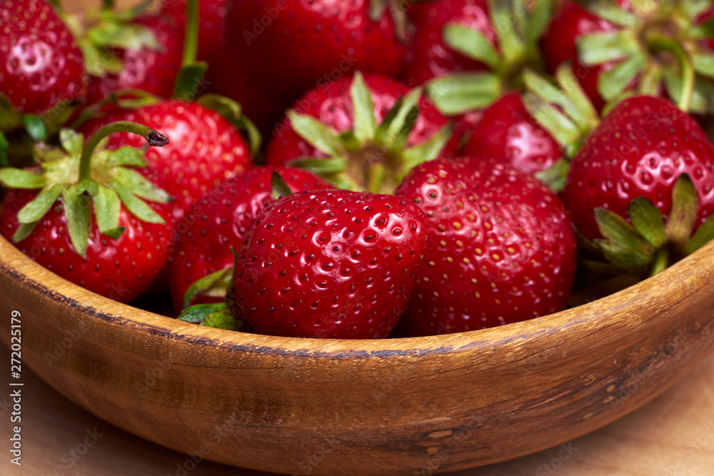 Close-up fresh strawberry in wooden bowl isolated on wooden background. Close-up fresh strawberry in wooden bowl isolated on wooden background.