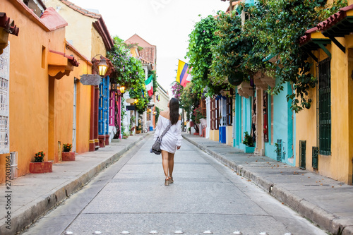 Beautiful woman on white dress walking alone at the colorful streets of the colonial walled city of Cartagena de Indias © anamejia18