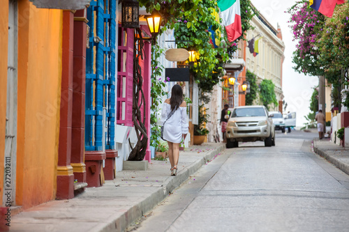 Beautiful woman on white dress walking alone at the colorful streets of the colonial walled city of Cartagena de Indias © anamejia18