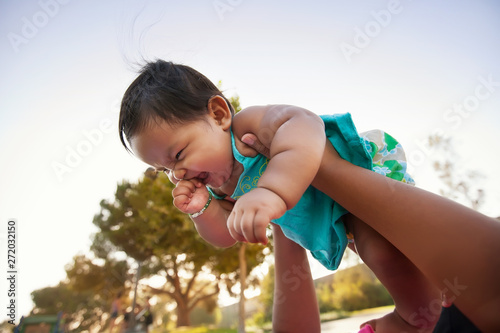 Baby girl being lifted up by mother into the sky, baby looks excited and nervous.