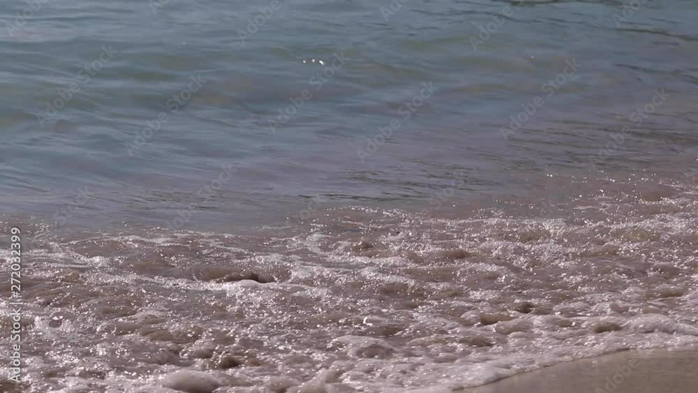 Slow motion shoot of sea waves moving over golden sandy beach in bright sunshine.Cagliari, Sardinia