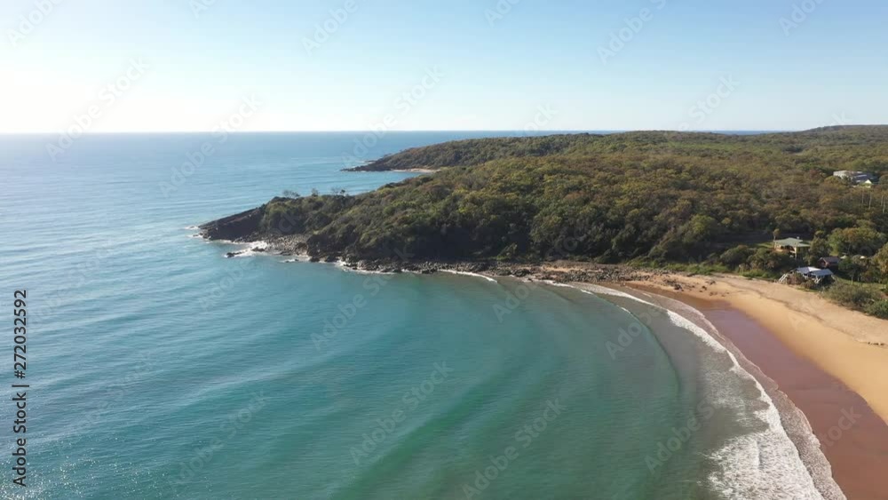 Aerial panning over a beautiful sand beach, blue turquoise ocean with gentle waves and nice green, rocky headland in the background. Tropical vibes Aerial panning over a beautiful sand beach, blue turquoise ocean with gentle waves and nice green, rocky headland in the background. Tropical vibes