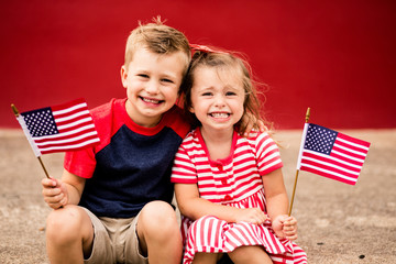 Cute siblings holding American flag while sitting on curb