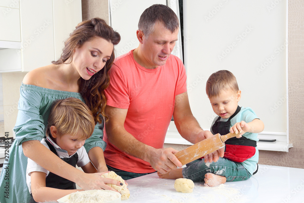 young parents help young sons knead the dough on the kitchen table. young parents help young sons knead the dough on the kitchen table.