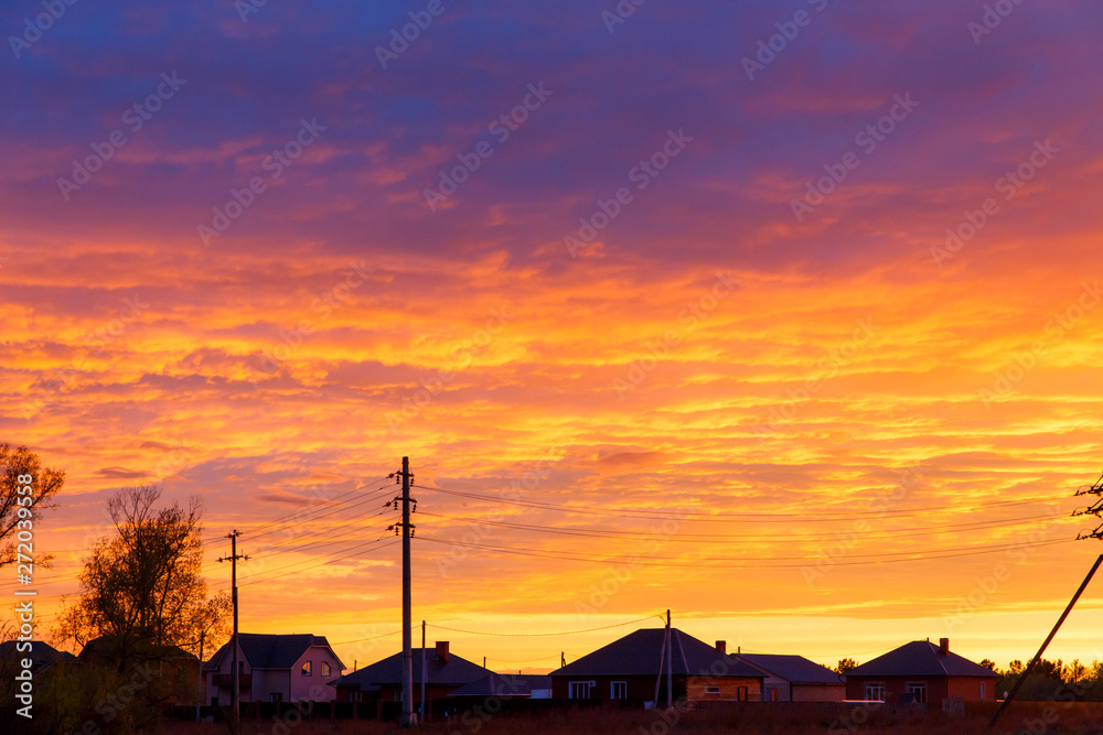 Colorful dramatic sky at sunset.  Bright blue orange background. The texture of the sunset. The sky at sunset as the sea and lava. The roofs of rural houses on the background of sunset.
