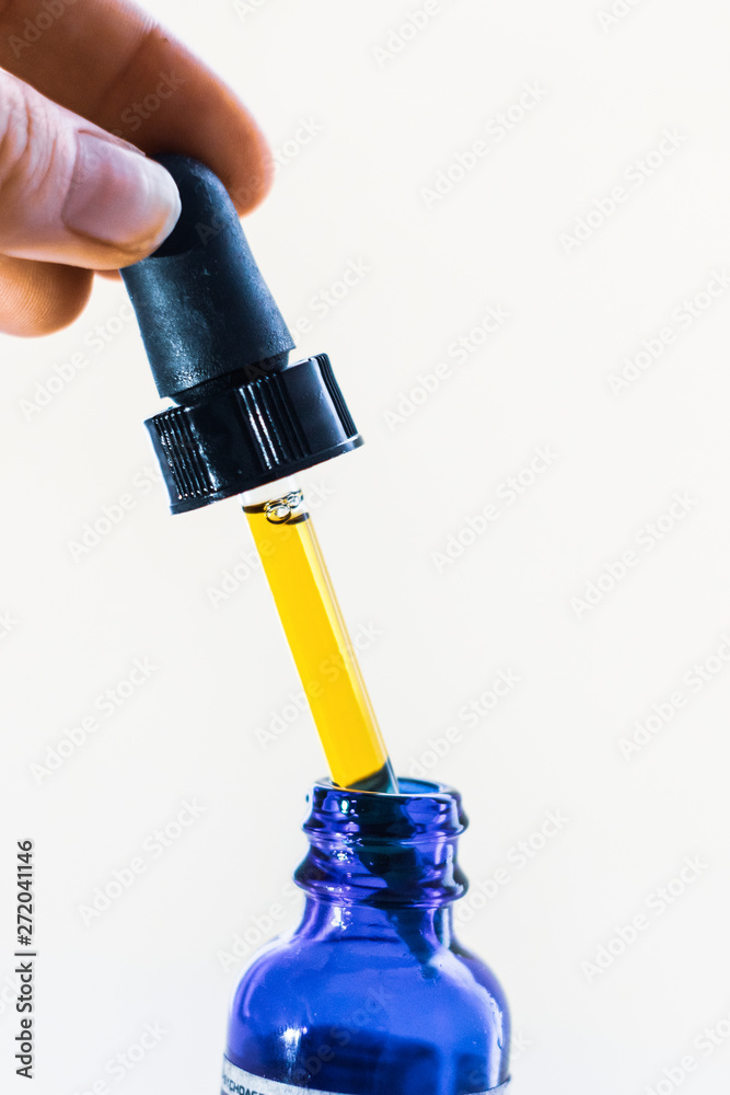 A dose of CBD tincture liquid being extracted from blue bottle with dropper. Up-close isolated on white background. A dose of CBD tincture liquid being extracted from blue bottle with dropper. Up-close isolated on white background.