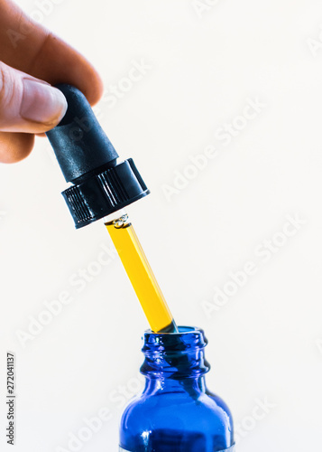 A dose of CBD tincture liquid being extracted from blue bottle with dropper. Up-close isolated on white background.