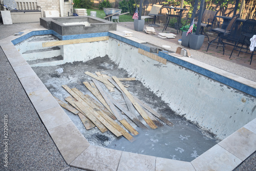 Empty swimming pool under remodel with new tile and coping with wooden debris 