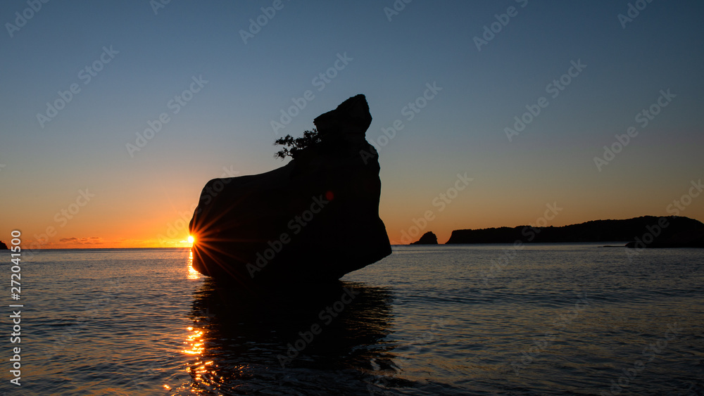 Silhouette rock at sunrise with shining starburst in Cathedral cove on the Coromandel Peninsula, New Zealand