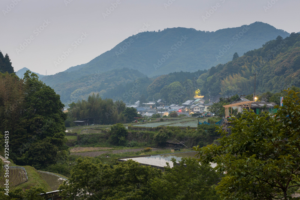 Fototapeta premium Rice fields and buildings in small Japanese mountain town at dusk