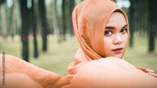 Картината върху платно Portrait of young muslim woman mellow yellow hijab over blurred the pine forest background