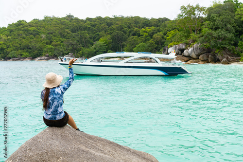 Young woman waving peace sign at yacht in blue water sea, with forest shoreline of exotic island © John