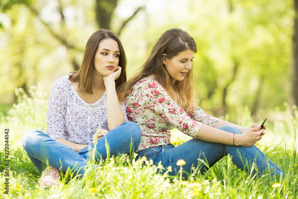 Two young women sitting outdoors and using phone Two young women sitting outdoors and using phone