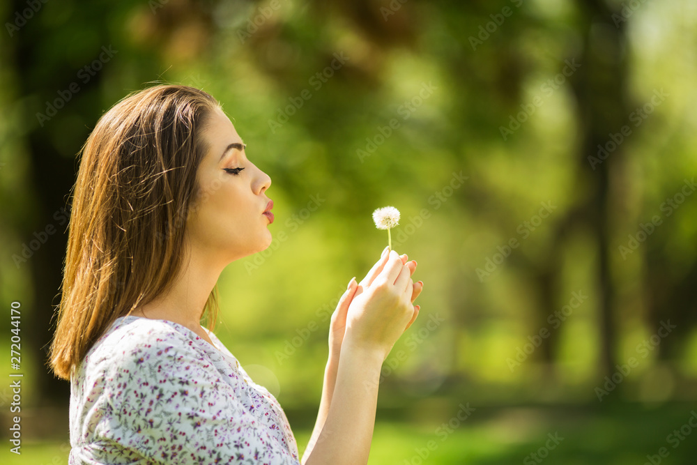 Beautiful young woman blowing dandelion
