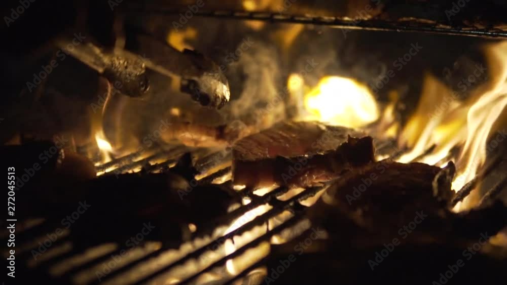 Close up on chefs hand turning over pork steak in flame. Slow motion Close up on chefs hand turning over pork steak in flame. Slow motion