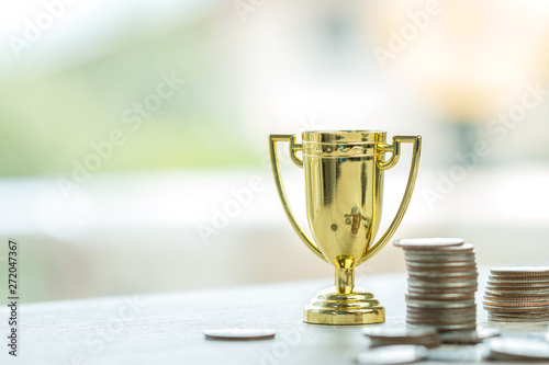 Golden trophy winner with rising money coins for business management profit target in life. Achievement success in currency economic for financial fund.